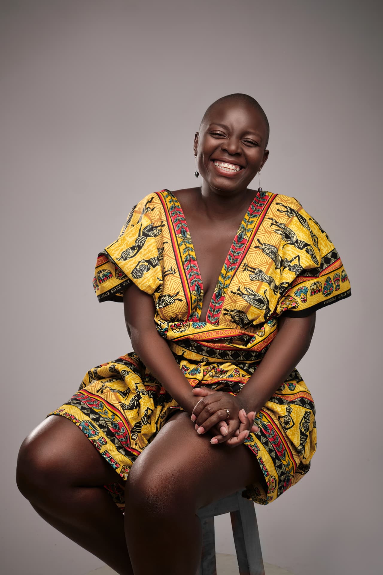 Énia Lipanga sorrindo, sentada num banco, com um vestido de capulana amarelo
